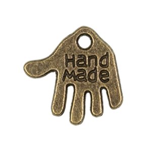 Das Bild zeigt eine kleine Hand aus silbernen Metall. Eingeprägt ist der Schriftzug Hand made. Am oberen Rand ist ein Loch zum Annaehen des Labels.